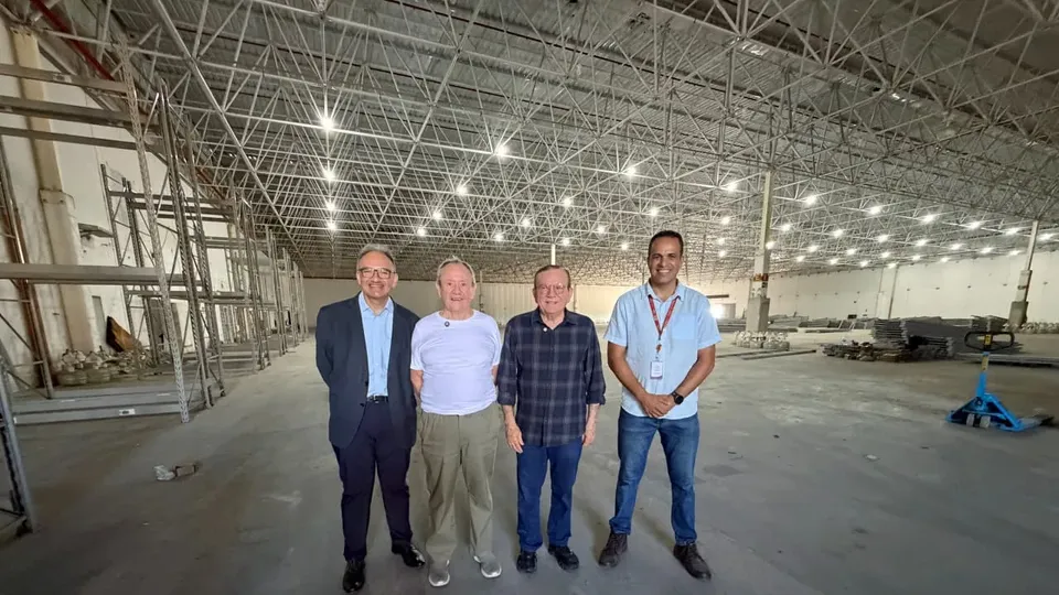 Quatro homens posam dentro de galpão amplo em montagem, com estrutura metálica no teto