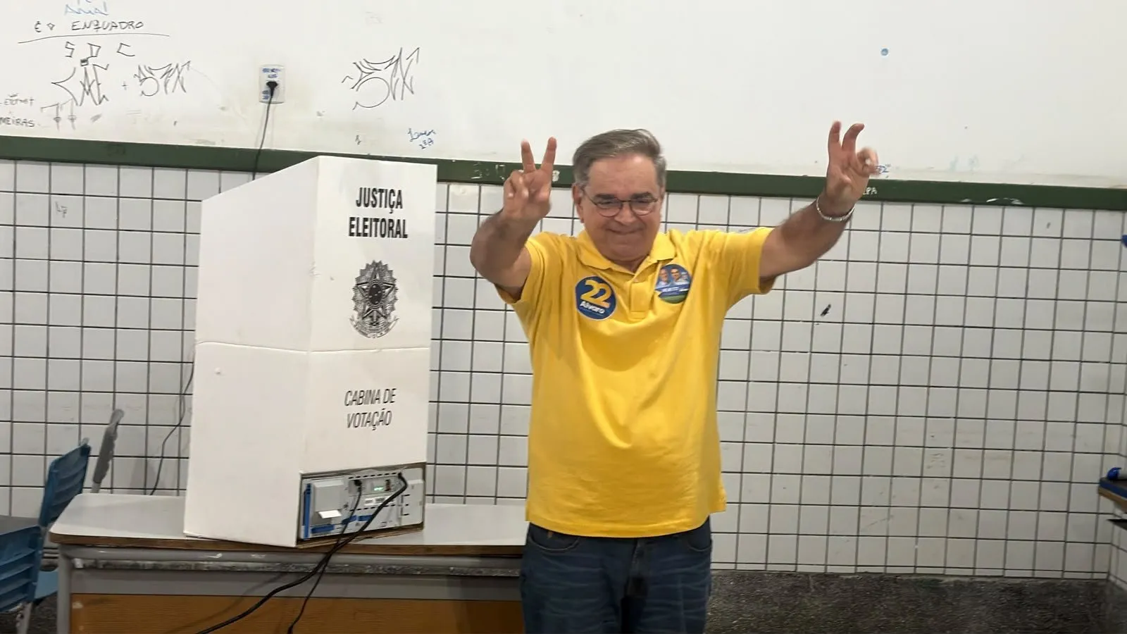 Álvaro Dias, de camisa amarela, faz sinal de vitória ao lado da cabine de votação