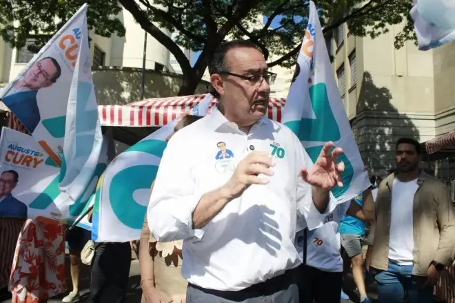 Augusto Cury, de camisa branca, fala com apoiadores na rua, com bandeiras da campanha