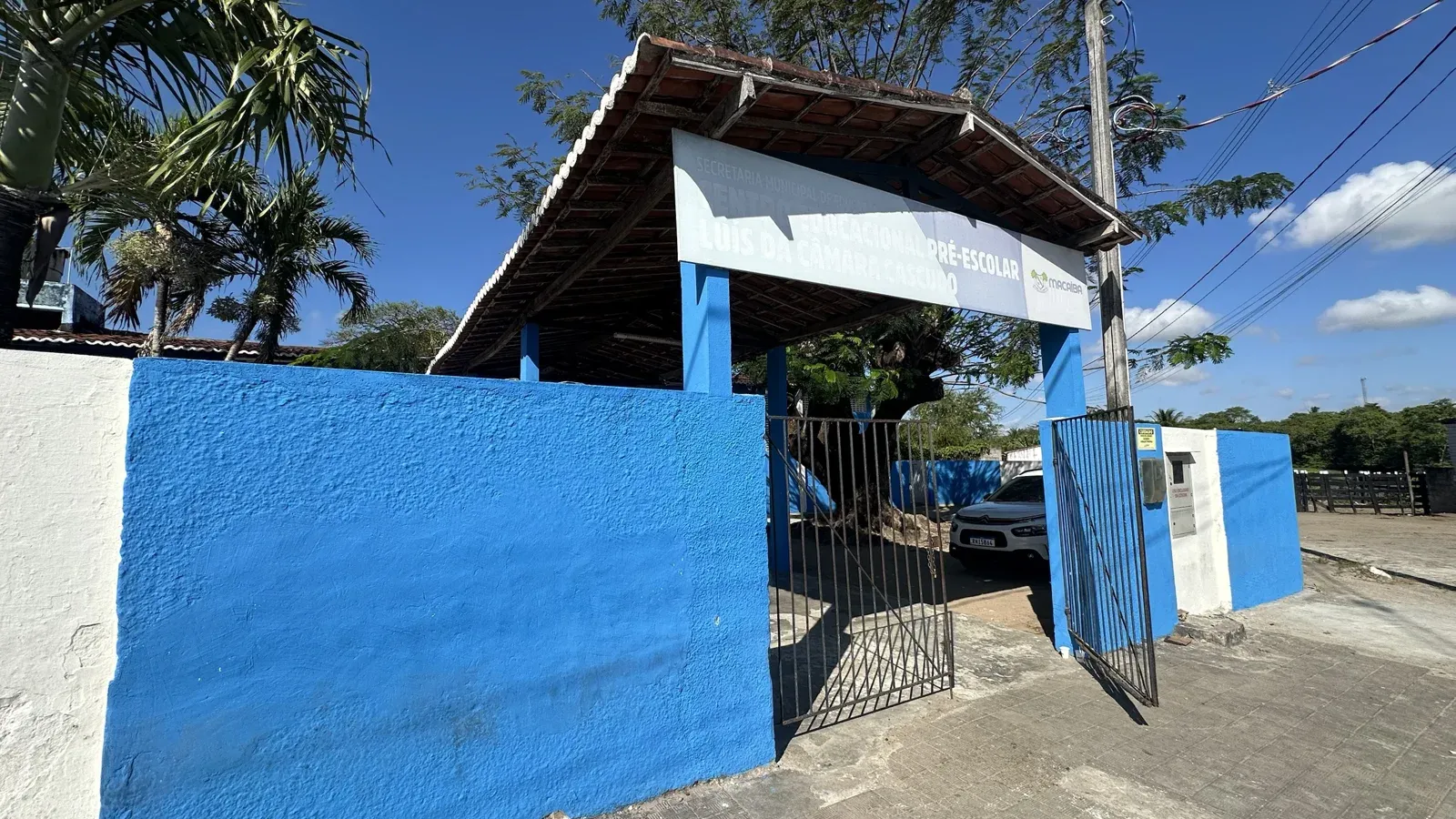Muro azul e portão aberto do Centro Educacional Pré-Escolar Luís da Câmara Cascudo, sem fila na entrada