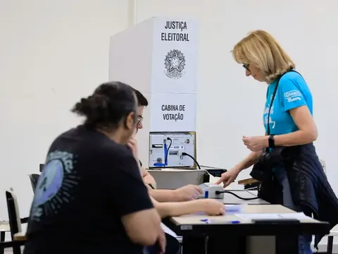 Eleitora se identifica com mesários ao lado da cabine de votação