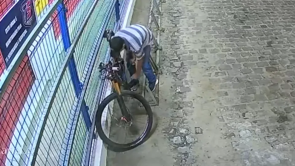 Imagem de câmera de segurança mostra homem mexendo no cadeado de uma bicicleta presa em um bicicletário