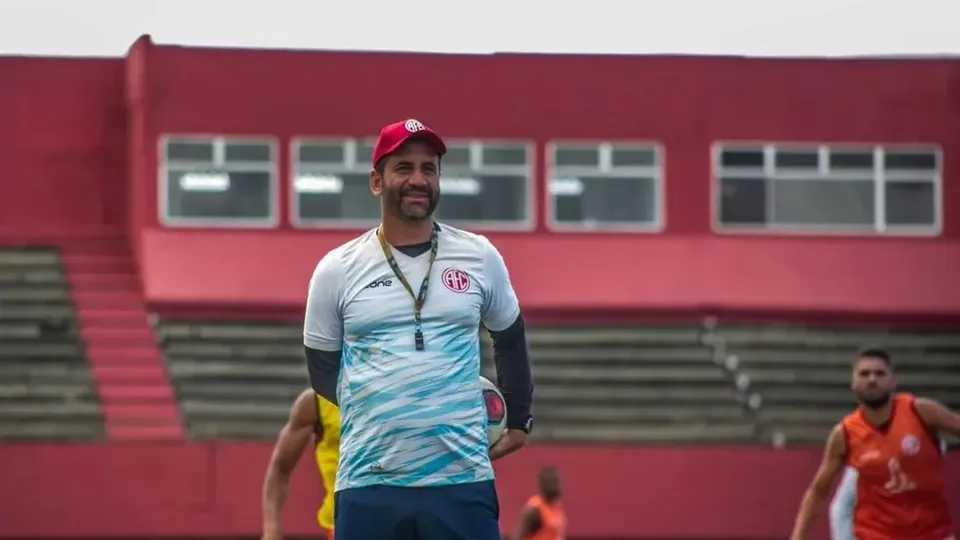 O técnico Hermes Júnior, de boné vermelho, à beira do campo durante um treino