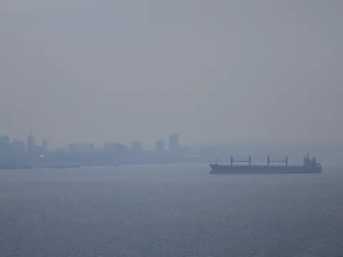 Prédios de Manaus quase sumindo na fumaça acinzentada, com um navio cargueiro no Rio Negro em primeiro plano