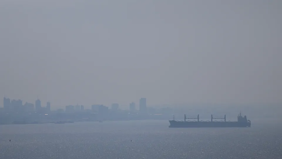 Prédios de Manaus quase sumindo na fumaça acinzentada, com um navio cargueiro no Rio Negro em primeiro plano