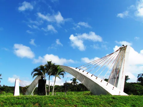 O Pórtico Augusto Severo inteiro, com o arco branco sustentado por cabos, sob céu azul