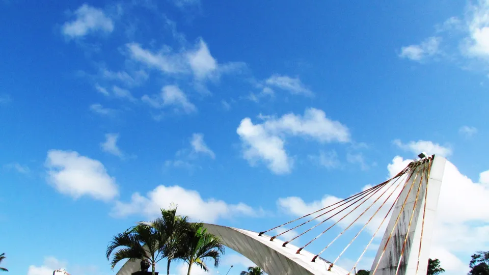 O Pórtico Augusto Severo inteiro, com o arco branco sustentado por cabos, sob céu azul