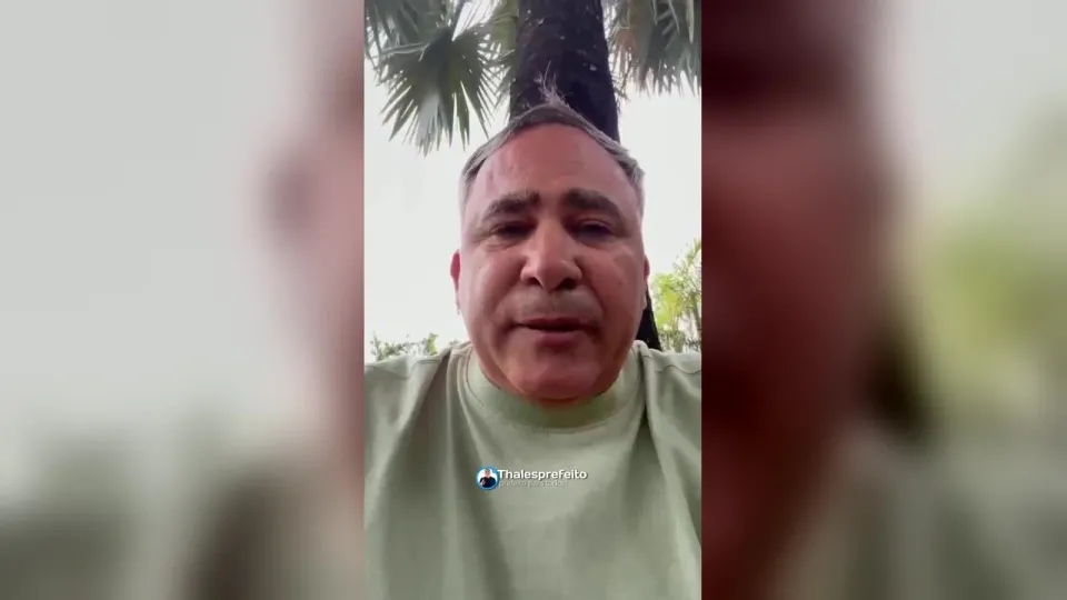 O prefeito Thales Farias, de camiseta verde-clara, grava vídeo ao ar livre com uma palmeira ao fundo
