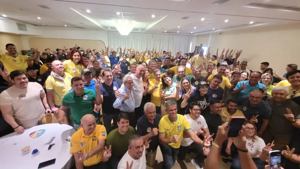 Salão de hotel cheio de prefeitos e lideranças, muitos de camisa amarela, com os braços erguidos