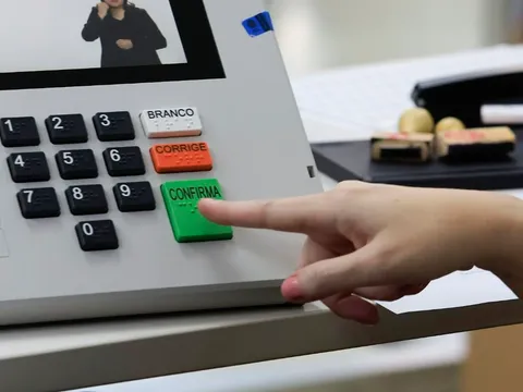 Dedo de eleitor prestes a apertar a tecla verde Confirma de uma urna eletrônica