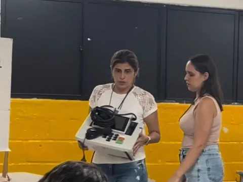 Mesária carrega a urna eletrônica com defeito ao lado da cabine de votação